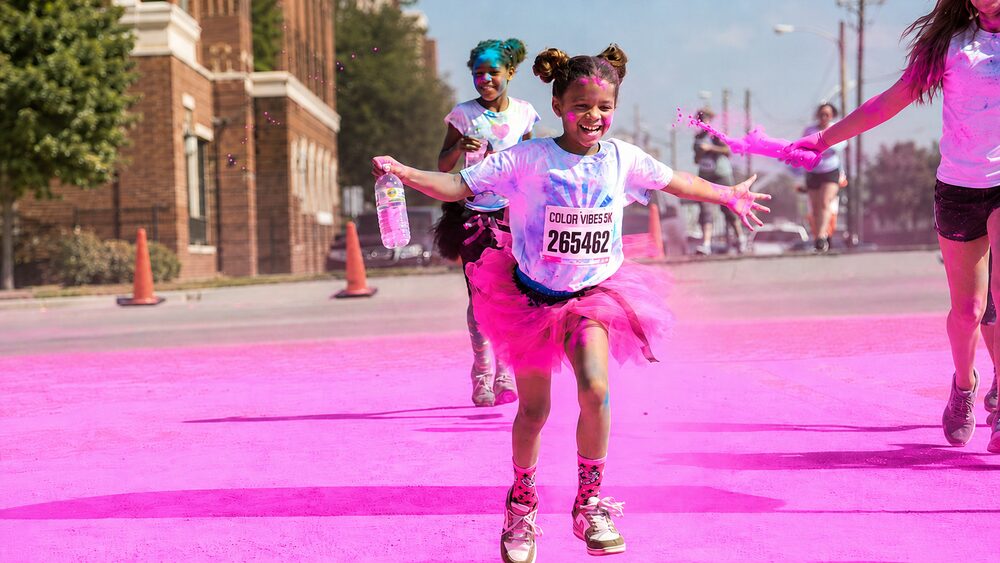 A young runner in a pink tutu laughing through pink color powder